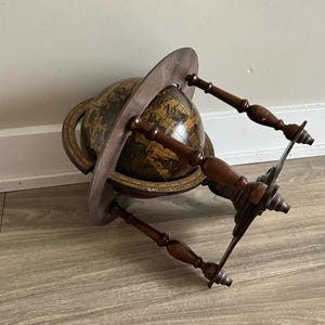 May include: An antique globe with a dark brown wooden stand and a circular frame. The globe features a detailed map with shades of brown and green. The stand has four wooden supports and a metal base.