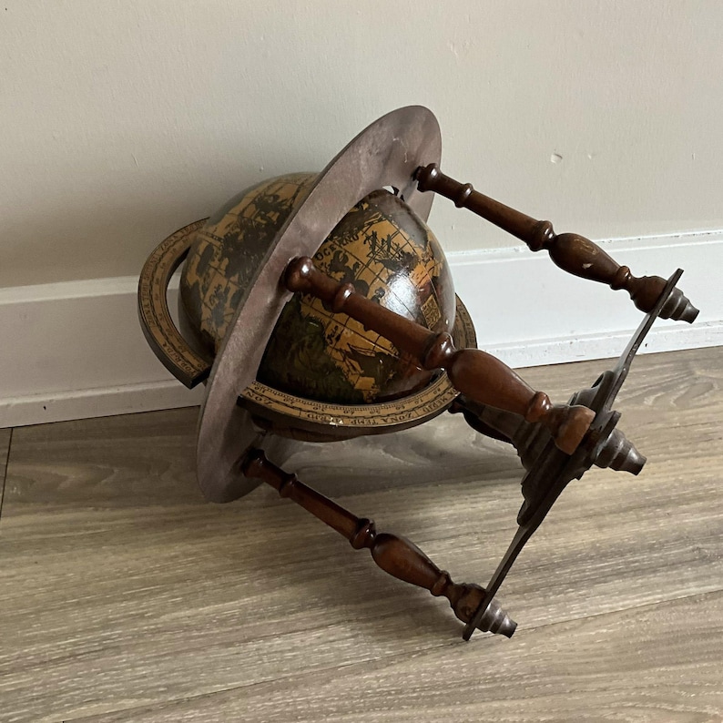 May include: An antique globe with a dark brown wooden stand and a circular frame. The globe features a detailed map with shades of brown and green. The stand has four wooden supports and a metal base.