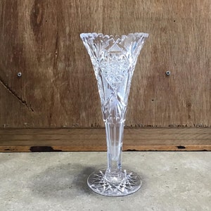 Könnte beinhalten: Eine klare Glasvase mit geschliffenem Glasdesign. Die Vase hat einen hohen, schlanken Körper und einen ausgestellten Boden.
