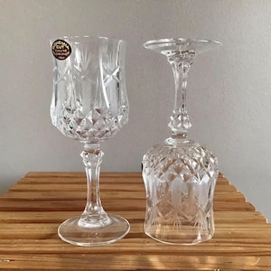 May include: Two clear glass wine glasses with intricate cut designs. The glass on the left has a label that reads "Bohemia Cut Genuine Lead Crystal Fine", the glass on the right has a wider bowl and a shorter stem.