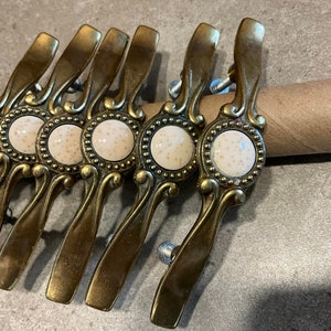 May include: A set of eight antique-style cabinet knobs with a gold finish and white porcelain inserts. Each knob features a decorative design with a scalloped edge.