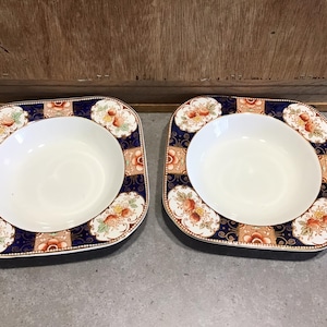 May include: Two square-shaped soup bowls with a white interior and a blue and gold floral pattern around the rim.