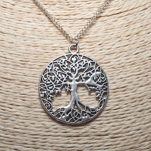 Könnte beinhalten: Silberfarbene Halskette mit einem Anhänger, der ein detailliertes Lebensbaum-Design in einem kreisförmigen Rahmen zeigt. Der Anhänger hängt an einer feinen Kette. Die Halskette wird auf einer neutralfarbenen Schaufensterpuppe präsentiert.
