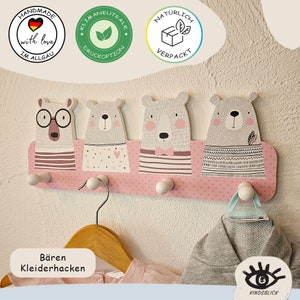 Könnte beinhalten: Rosa Holz-Kleiderhaken in Form von Bären mit vier Haken. Der Kleiderhaken hat ein Punkte-Muster und jeder Bär hat ein anderes Design. Der Text "Bären Kleiderhacken" ist unter dem Kleiderhaken sichtbar.
