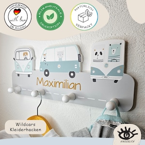 Könnte beinhalten: Eine graue Wandgarderobe mit drei illustrierten hellblauen Campingbussen mit tierischen Fahrern. Der Name Maximilian ist in goldener Schrift auf der Vorderseite aufgedruckt. Vier weiße Holzkugeln dienen als Haken zum Aufhängen.