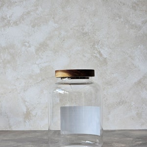 May include: A clear glass jar with a wooden lid. The jar has a white label with the text "ROOT" on it.