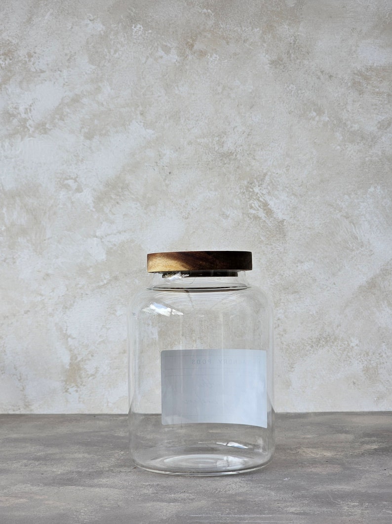 May include: A clear glass jar with a wooden lid. The jar has a white label with the text "ROOT" on it.