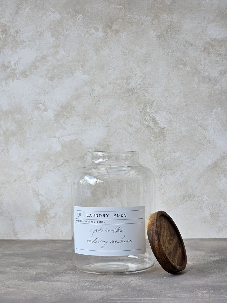 May include: A clear glass jar with a wooden lid, labelled "Laundry Pods" with the washing instructions "1 pod in the washing machine".
