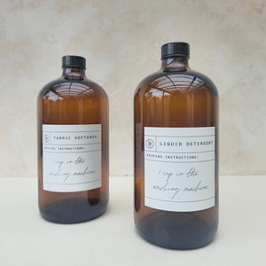 May include: Two amber glass bottles with black lids. One is labelled "FABRIC SOFTENER" and the other "LIQUID DETERGENT". Both have white labels with washing instructions: "1 cup in the washing machine."