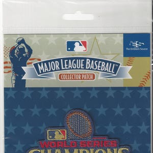 Può includere: Una toppa ricamata blu e oro con il testo "World Series Champions 2020 LA 2024" e un logo di baseball. La toppa è su uno sfondo blu con stelle bianche.