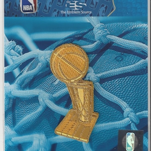 May include: A gold NBA championship trophy patch with a basketball on top. The patch is on a blue background with a repeating pattern of NBA logos. The text "COLLECTOR PATCH" is at the top of the image. The text "Officially Licensed NBA Collector Patch" is in a red box below the title. The text "The Emblem Source" is below the red box.