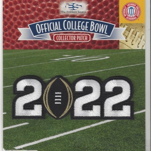 May include: A black and white patch with the number 2022 and a gold football in the centre. The patch is on a green and white football field background. The text "Official College Bowl Collector Patch" is at the top of the image.
