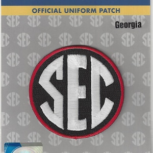 May include: Official uniform patch featuring the SEC logo. The patch has a black background with a red border and white embroidered letters. The text "Georgia" is above the logo. The patch is on a card with the text "Southeastern Conference".