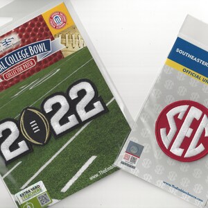 May include: Two embroidered patches, one with the number 2022 and a football, and the other with the SEC logo in white on a red circle. Both patches are on white backgrounds with text that reads "Official College Bowl Collector Patch" and "Southeastern Conference Official Uniform Patch Alabama".