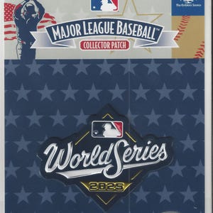 Könnte beinhalten: Ein Major League Baseball Sammler-Patch mit dem World Series Logo für 2025. Der Patch befindet sich in einer transparenten Kunststoffverpackung mit blauem Hintergrund und Sternmuster. Enthält das MLB-Logo und "Genuine Merchandise".