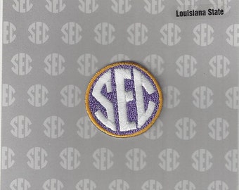 Op de afbeelding: Een wit en paarse SEC-logo patch met een gouden rand. De patch bevindt zich op een grijze achtergrond met een herhalend patroon van het SEC-logo. De tekst "Louisiana State" is in zwart bovenaan de afbeelding gedrukt. De tekst "OFFICIAL UNIFORM PATCH" is in zwart boven het logo gedrukt. De tekst "SOUTHEASTERN SEC CONFERENCE" is in zwart bovenaan de afbeelding gedrukt.