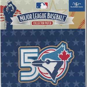 Könnte beinhalten: Ein Major League Baseball Sammler-Patch mit dem Logo der Toronto Blue Jays, einer großen "50" und einem Baseball. Der Patch befindet sich in einer transparenten Plastikhülle. Der Hintergrund ist blau mit weißen Sternen.