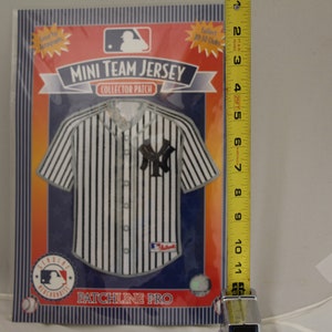 Peut inclure: Un maillot de baseball rayé blanc et noir avec le logo des New York Yankees. Le maillot est un mini maillot de collection avec un patch. L'emballage est rouge, orange et bleu avec le texte "MINI TEAM JERSEY COLLECTOR PATCH" et "PATCHLINE PRO".