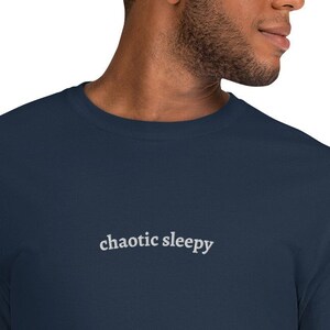 May include: A navy blue long-sleeve sweatshirt with the words "chaotic sleepy" embroidered in white. The sweatshirt is made of a soft material and has a crew neck.