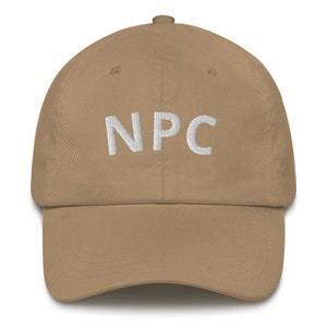 Puede incluir: Gorra de béisbol color beige con las letras "NPC" bordadas en blanco en la parte delantera. La gorra tiene una visera curva y un cierre de correa de tela en la parte trasera.