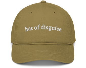 May include: A khaki colored baseball cap with the text "hat of disguise" embroidered in white on the front.