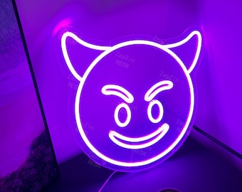 May include: A white neon sign shaped like a devil emoji with a mischievous grin. The sign is lit up in a bright purple color and has the text "ZapZin NEON" printed on it.