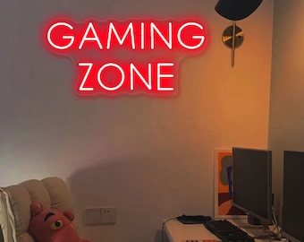 May include: Red neon sign with the words "GAMING ZONE" on a white wall. The sign is in a room with a desk, two computer monitors, and a chair.