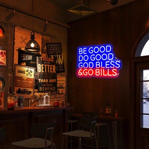 May include: A neon sign with the words "BE GOOD DO GOOD GOD BLESS & GO BILLS" in blue and red. The sign is mounted on a wooden wall in a bar setting, with vintage posters and a bar counter visible.