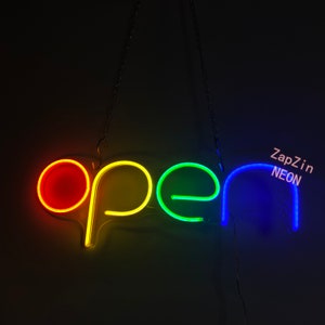 May include: A neon sign that says "OPEN" in rainbow colors. The sign is hanging from a chain and has a white background.