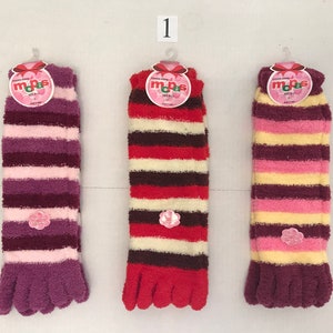 May include: Three pairs of fuzzy striped socks with toe separators. The socks are pink, red, and yellow with brown stripes. Each sock has a pink flower tag with the word "mops" on it.