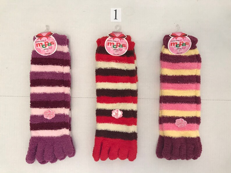 May include: Three pairs of fuzzy striped socks with toe separators. The socks are pink, red, and yellow with brown stripes. Each sock has a pink flower tag with the word "mops" on it.