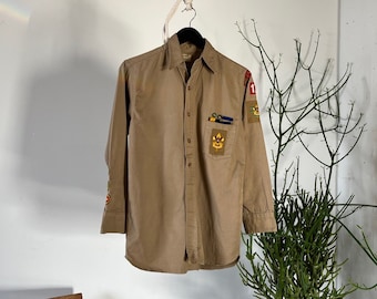 May include: A tan long-sleeve shirt with embroidered patches and a button-up front.