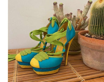 May include: A pair of blue and yellow platform heels with green ribbon laces. The heels are on a woven wicker surface.