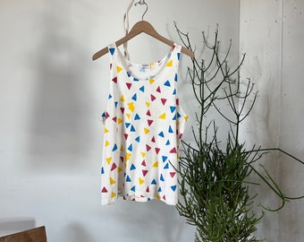 May include: White tank top with a colorful geometric pattern of red, yellow, and blue triangles.