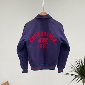 Könnte beinhalten: Eine violette Collegejacke mit roten und weißen Stickereien, auf denen "East Orange H.S." steht.