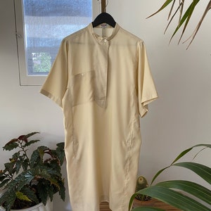 May include: A pale yellow short-sleeved collared shirt with a button-up front and a single pocket on the left side.