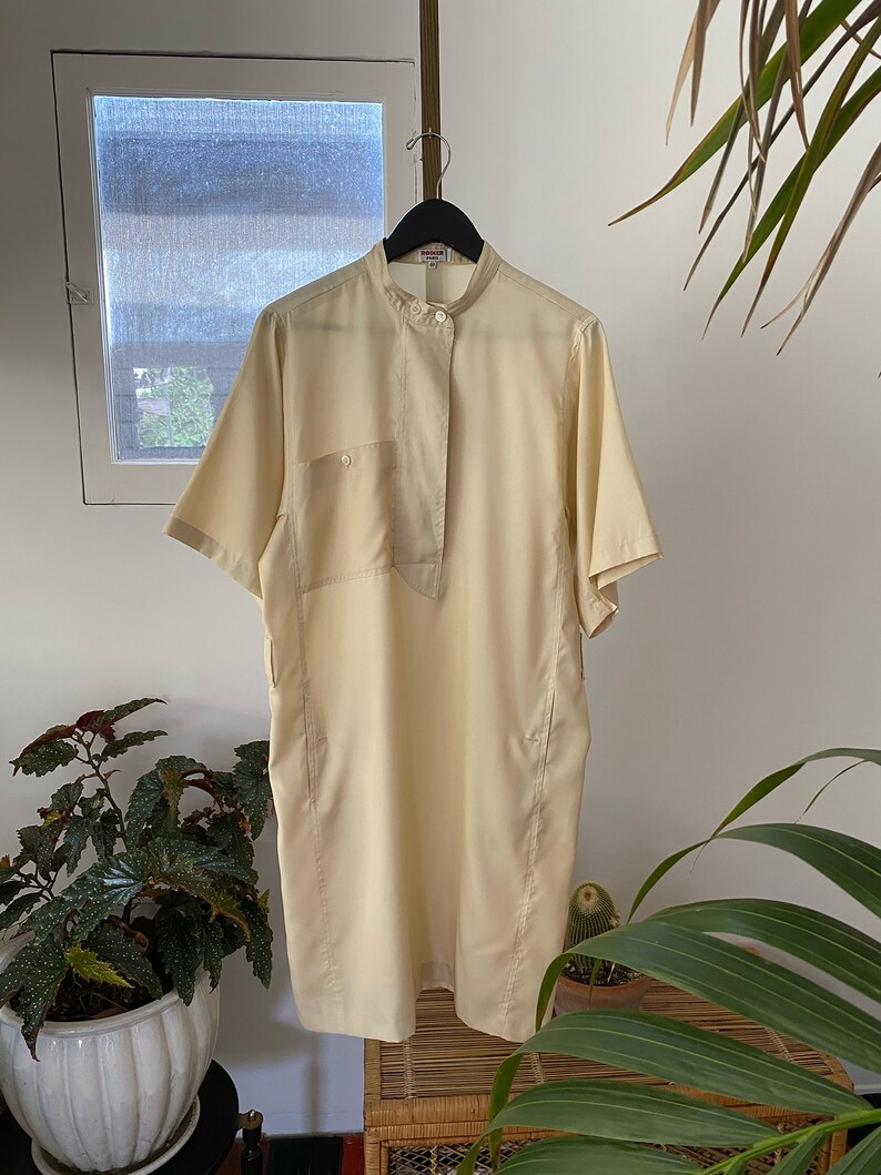May include: A pale yellow short-sleeved collared shirt with a button-up front and a single pocket on the left side.