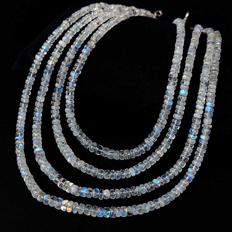 Puede incluir: Cinco hilos de collares de piedras preciosas claras y facetadas con un sutil brillo iridiscente. Las cuentas est&aacute;n ensartadas, creando un efecto en capas. El fondo es negro, resaltando los collares.