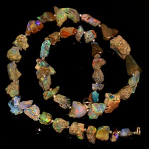 May include: A necklace composed of irregularly shaped, raw opal stones. The opals display a variety of colors, including blue, green, orange, and brown, with flashes of iridescence. The stones are strung together with small silver beads.
