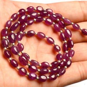 May include: A strand of purple gemstone beads with silver spacer beads. The beads are oval shaped and have a smooth, polished finish.