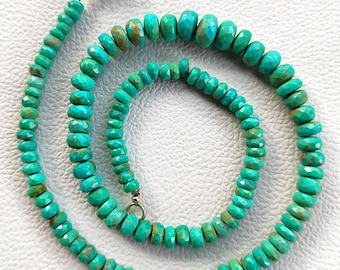 May include: A turquoise gemstone necklace with a silver clasp. The necklace is composed of faceted, oval-shaped beads in varying sizes. The beads are a vibrant turquoise color with brown matrix patterns. The necklace is displayed on a white surface.