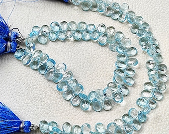 May include: A strand of light blue gemstone beads, with a teardrop shape, strung on a cord with blue tassels at each end.