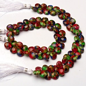 Pode incluir: Um fio de contas de pedras preciosas coloridas com manchas douradas. As contas são uma mistura de vermelho, verde e azul, e todas são redondas e lisas. As contas são enfiadas em um cordão branco com borlas em cada extremidade.