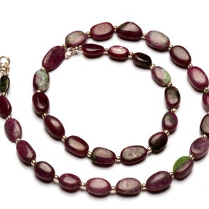 May include: A necklace made of oval-shaped, red and green gemstone beads with gold accents.