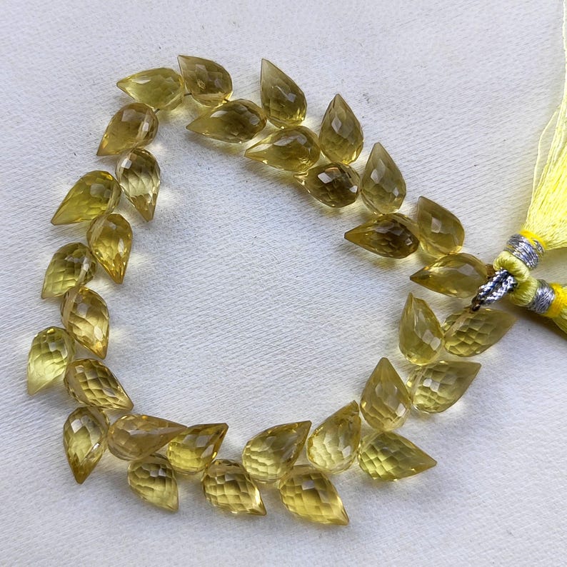 May include: A strand of 30 faceted teardrop-shaped beads in a light yellow color. The beads are strung on a clear thread and are arranged in a circular pattern.
