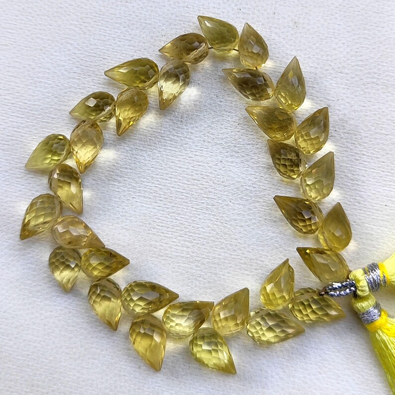 May include: A strand of 20 faceted teardrop-shaped beads made of yellow citrine. The beads are strung on a wire and have a tassel at the end.