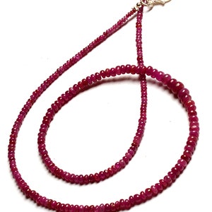 Op de afbeelding: Een lange ketting gemaakt van kleine, ronde, rode robijn kralen. De ketting heeft een zilveren sluiting.