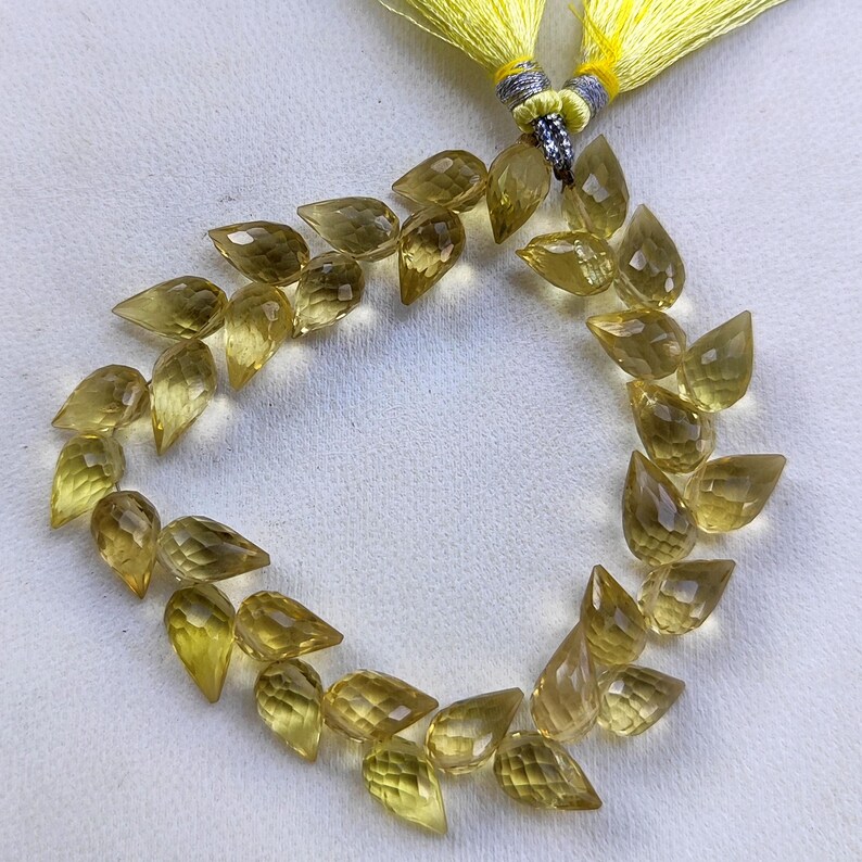May include: A strand of yellow faceted teardrop-shaped beads, strung on a thin cord. The beads are arranged in a circular pattern, with the cord tied off at the top.
