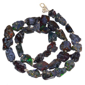 May include: A necklace composed of irregularly shaped, dark blue and black opal stones. The stones display flashes of green, red, and gold. The necklace is strung with small silver beads and has a silver clasp.