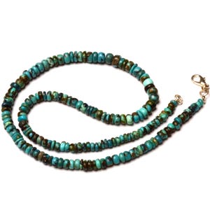 May include: A turquoise beaded necklace with a silver clasp. The necklace features small, round beads in shades of turquoise and brown. The beads are strung together to form a necklace.